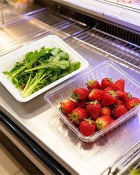 Fresh strawberries and greens in clamshell packaging on a refrigerated shelf